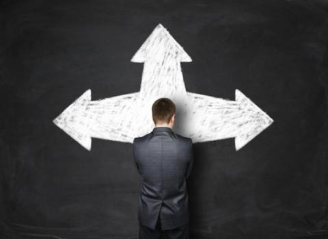 Businessman standing behind black wall with arrows pointing at different directions