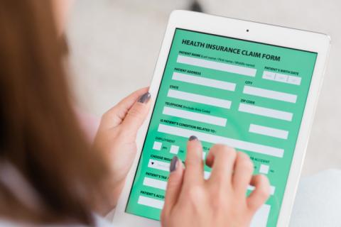 Hands of young woman holding touchpad with health insurance form while filling in personal information