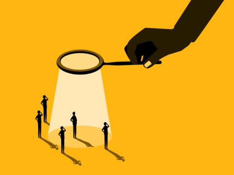 An illustration featuring a hand holding a magnifying glass, casting a spotlight on one of several silhouetted figures standing on a yellow background. 